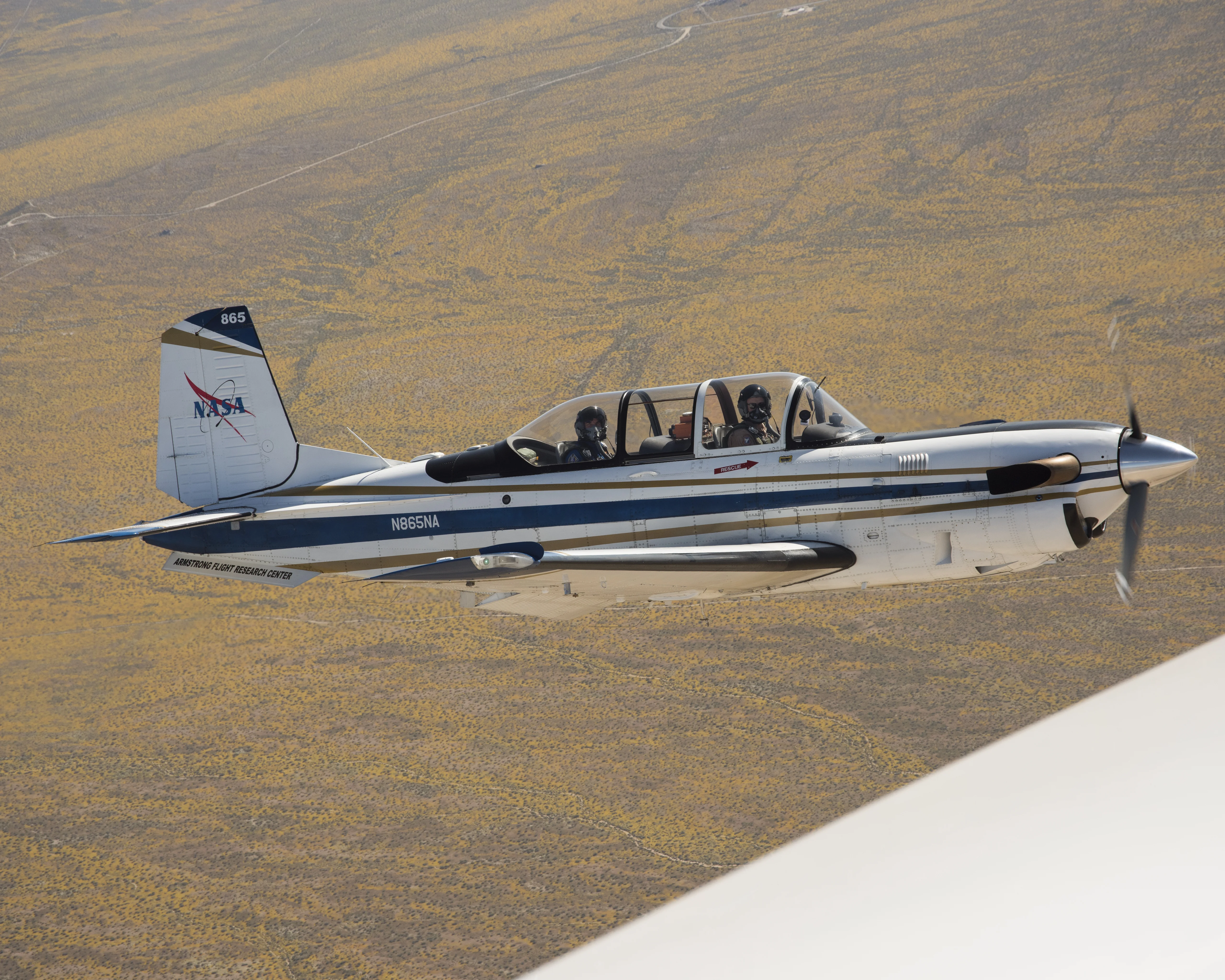 NASA Aircraft flies over yellow wildflowers abundant due to rainy winter season. The T-34 aircraft was flown from the agency's Armstrong Flight Research Center.